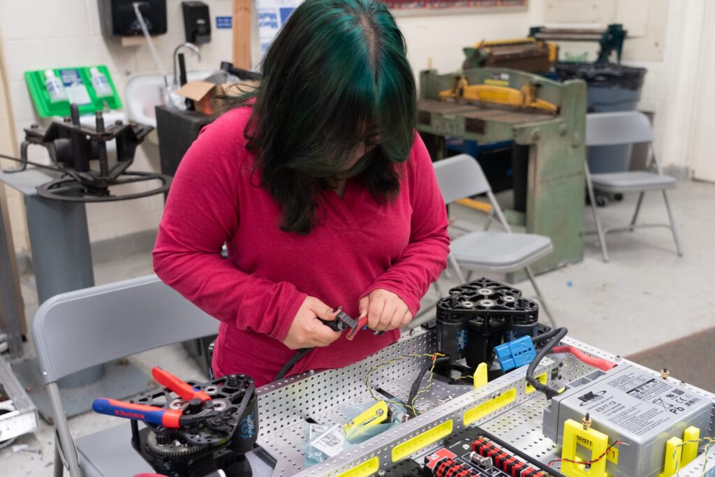 A student assembling a robot component at a workbench in the robotics shop