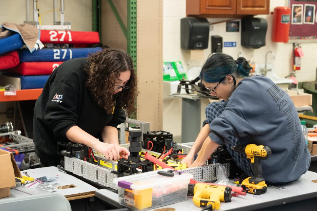 Two students building a robot chassis on a workbench in the robotics shop