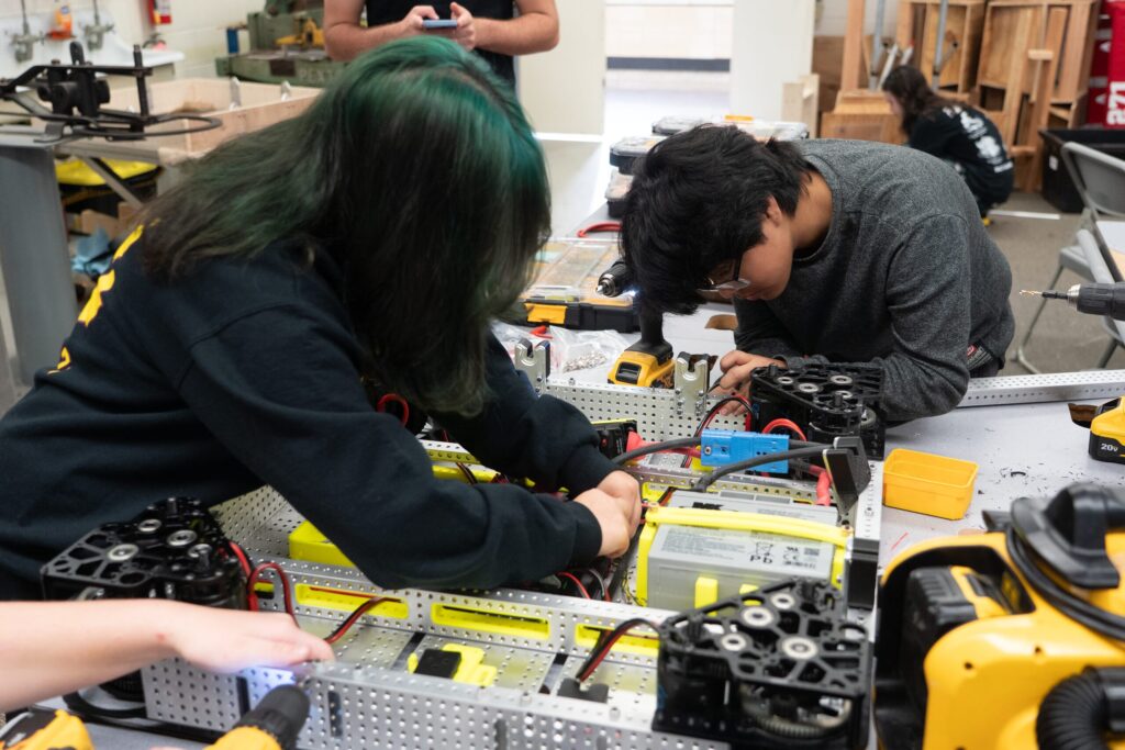Students wiring robot electronics at a workbench