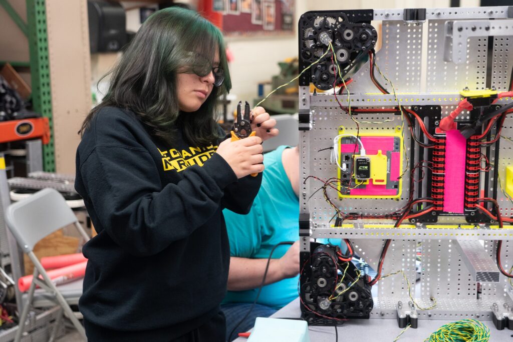A student wiring a robot control board, with a close-up of the finished electronics panel