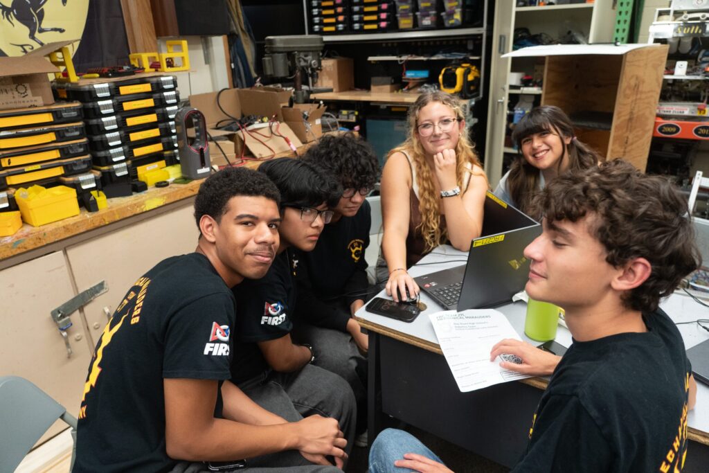 Students gathered around a laptop in the Team 271 robotics workshop
